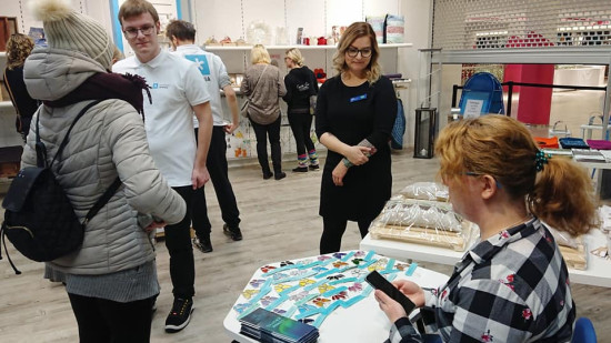 Ihmisiä ostoksilla puodissa, pöydän takana käsitöiden esittelijä.