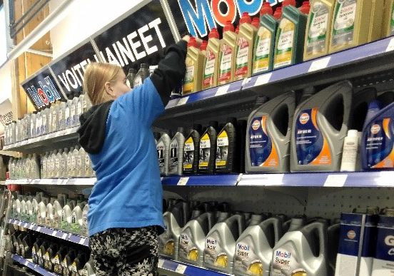 Tyttö hyllyttää moottoriöljyjä kaupassa ylimmälle hyllylle.