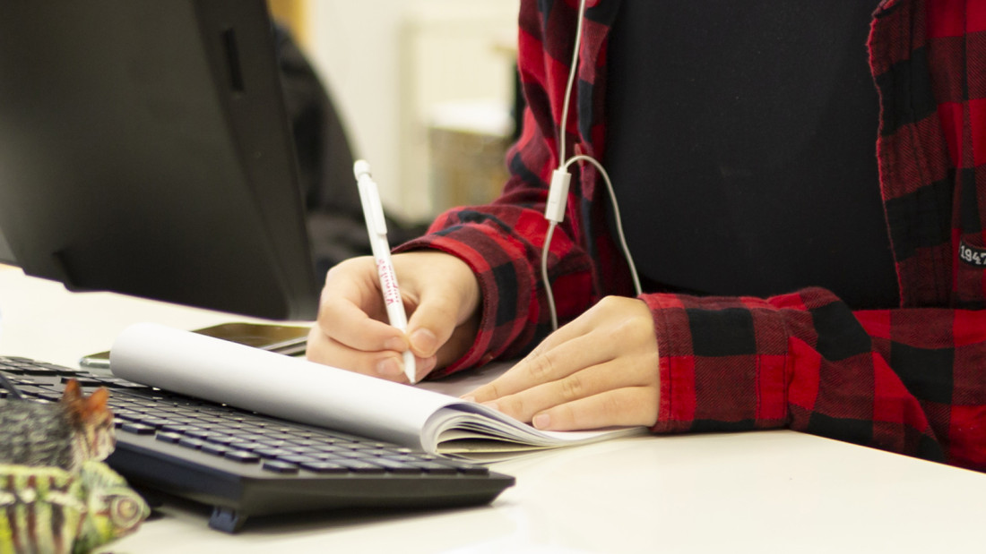 Kynällä paperille kirjoittavat kädet, vieressä tietokoneen näppäimistö.