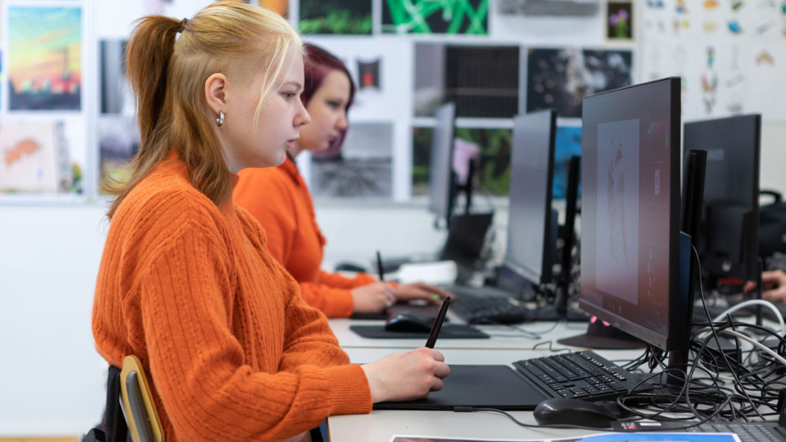 Kaksi nuorta naista istuu luokassa ja piirtää tietokoneelle piirtopöydän avulla.