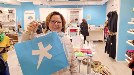 Näkymä Spesia Puotiin, etualalla nainen esittelee paperista ostoskassia, jossa sinisellä pohjalla valkoinen Spesia-tähti.