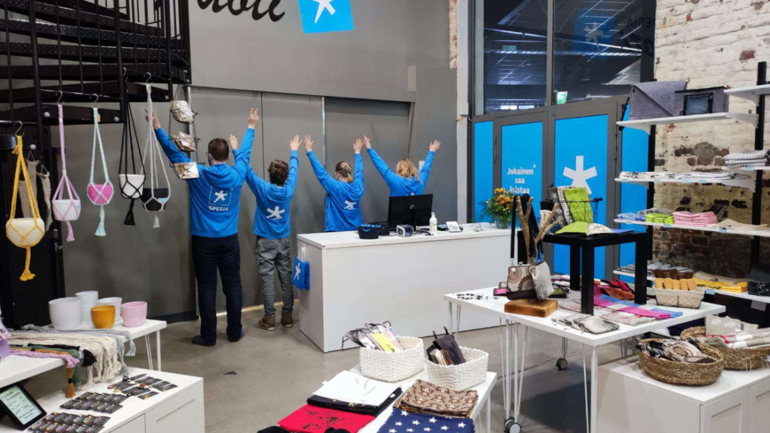 Yleiskuva Spesia Puodista, jonka takaosassa kassan takana seisoo spesialaisia sinisissä huppareissa kädet kohotettuina.