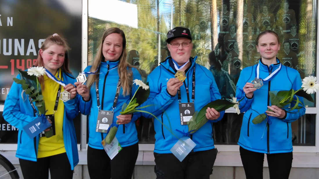 Spesian Taitaja-mitalistit rivissä sinisissä huppareissa, onnittelukukat käsissään.