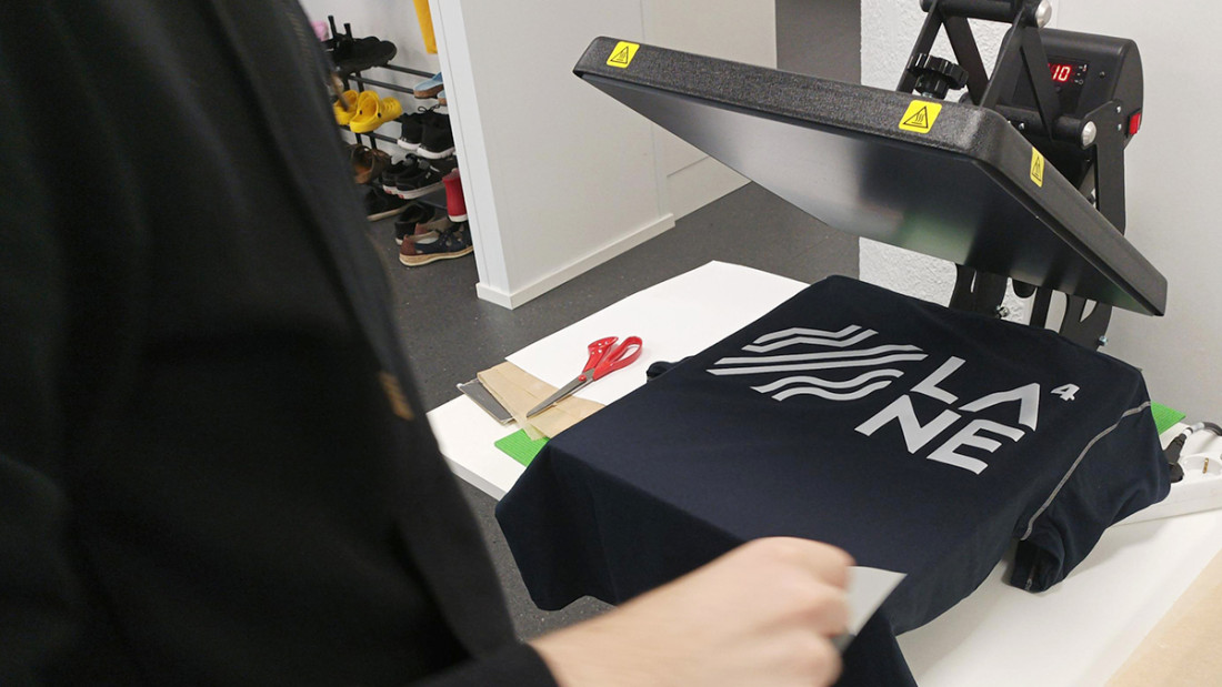 Kankaanpainantaa prässillä, etualalla näkyy henkilö osittain.