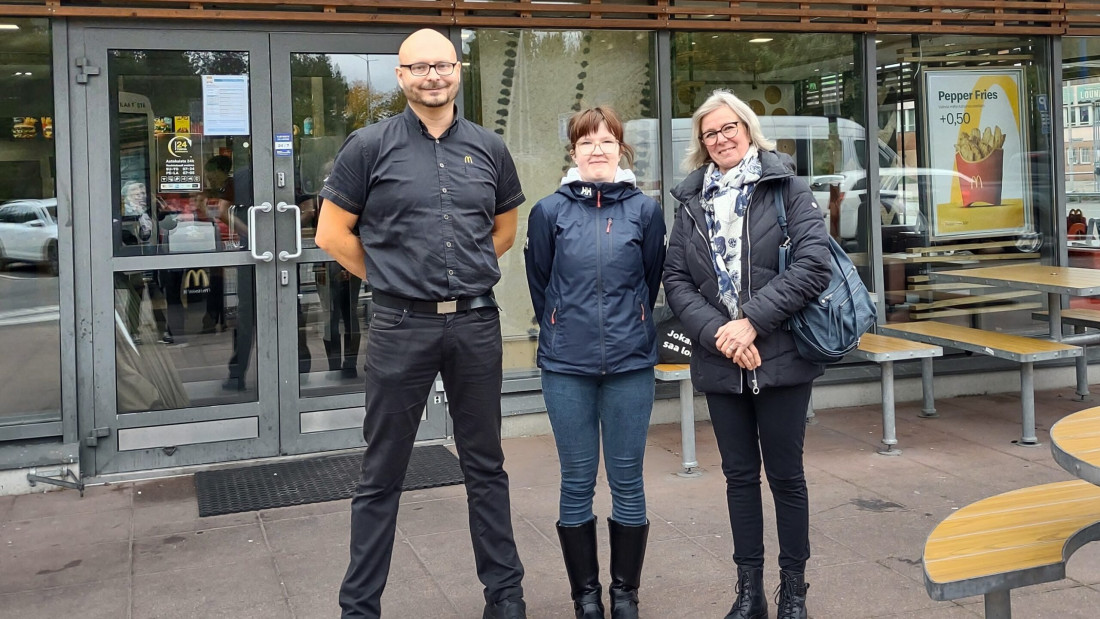 Mies ja kaksi naista seisovat rinnakkain, ulkona McDonaldsin edessä.