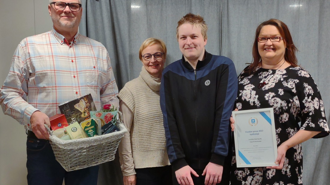 Kolme aikuista ja yksi nuori seisovat vierekäin, yhdellä kädessä herkkukori ja yhdellä diplomi.