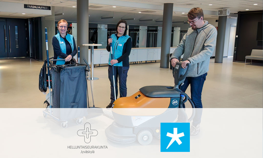 Kaksi naista ja mies aulassa siivouskärryn ja lattianpesukoneen takana.