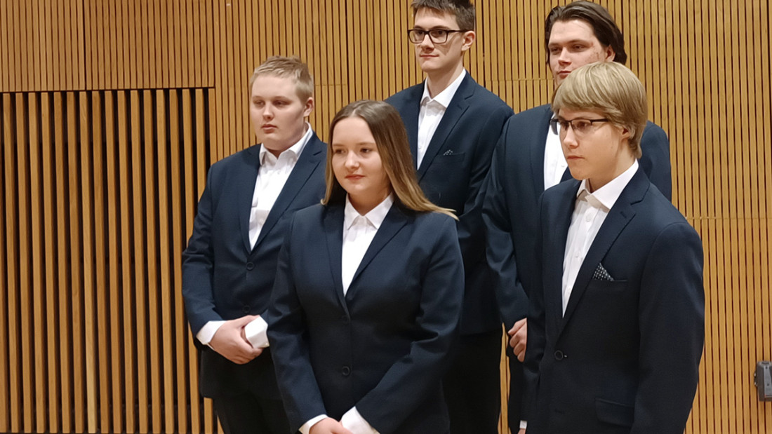 Neljä kilpailijaa virallisissa tyylikkäissä edustuspuvuissa valkoisine kauluspaitoineen.