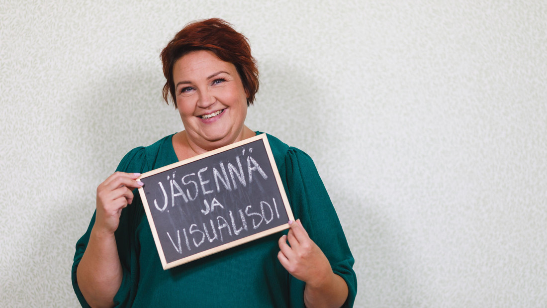 Marika Mäkinen pitelee liitutaulua, jossa on teksti Jäennä ja visualisoi.