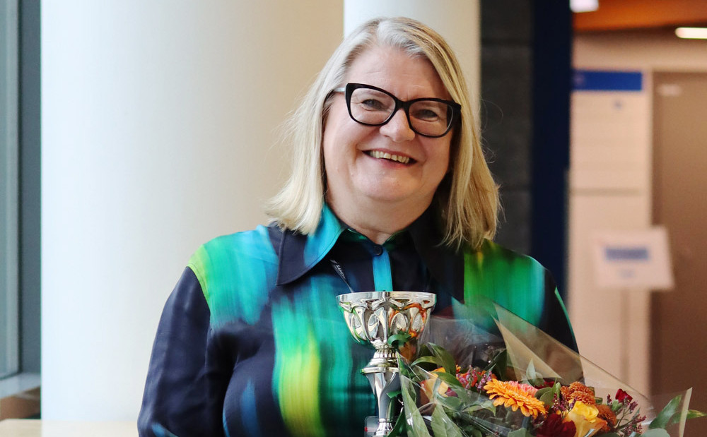 Rehtori Tiina Meriläinen hymyilee pokaali ja kukkakimppu kädessään.