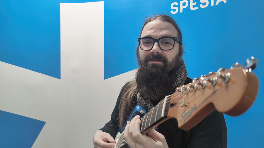 Heikki Mäkinen soittaa kitaraa. Sininen tausta jossa iso valkoinen Spesian tähti ja teksti Ammattiopisto Spesia.