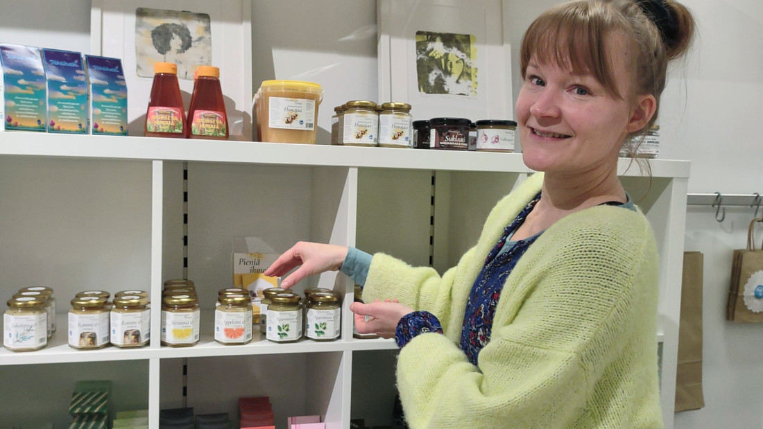 Johanna Purokari järjestelee Spesia Puodin myytävien tuotteiden hyllyä ja hymyilee kameralle.