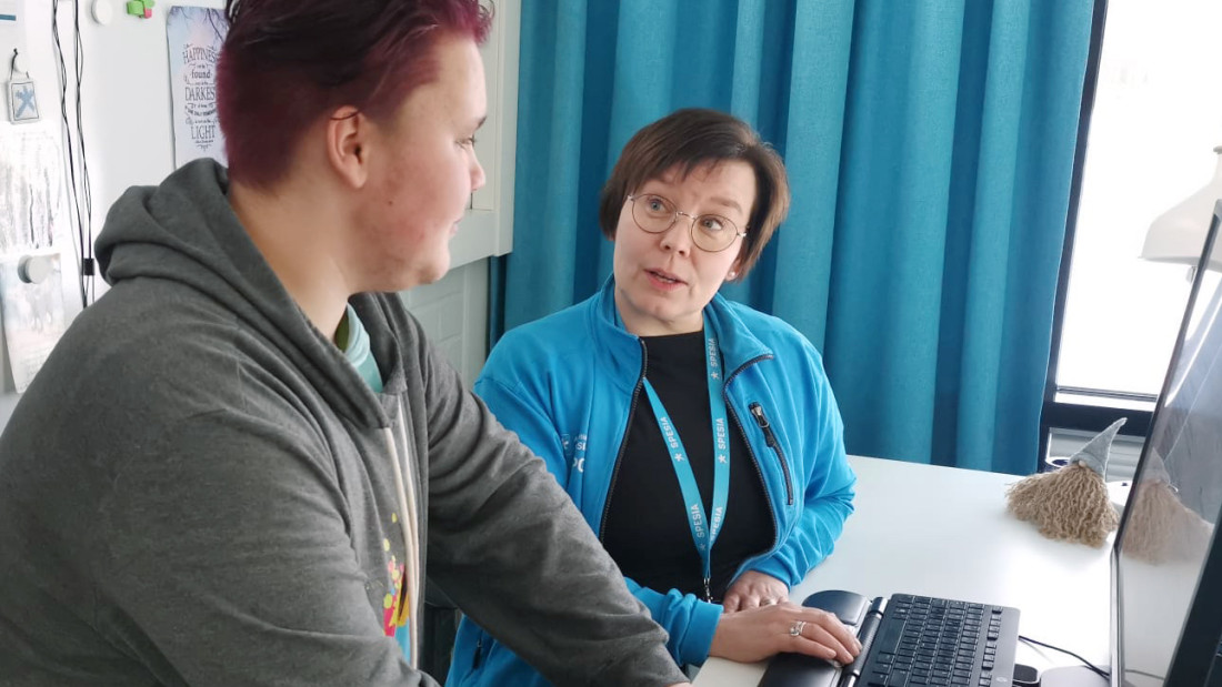 Opo Kati keskustelee tietokoneen äärellä opiskelijan kanssa, päällään Spesian sininen huppari.