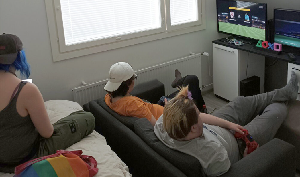 Opiskelijoita löhöää asuntolan sohvalla pelaten tietokonepeliä.