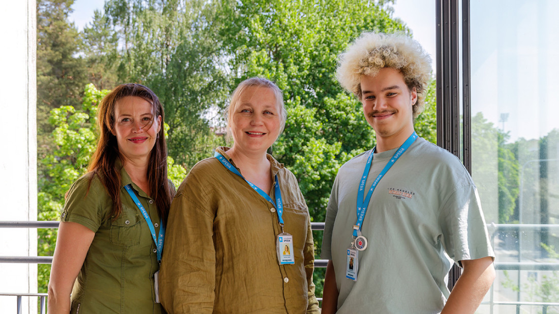 Kolme henkilöä seisoo rinnakkain ja katsoo kameraan. Kaikilla on Spesian kaulanauha ja henkilökortti kaulassaan.