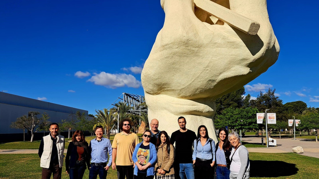 Ryhmäkuvassa taustalla patsas, joka on suuri käsi pitelemässä kynää valmiina kirjoittamaan.