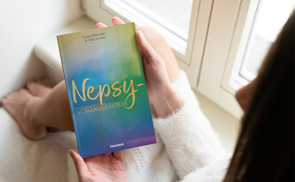 Nainen istuu ikkunalaudalla ja pitelee käsissään Nepsy-voimavarakirjaa.