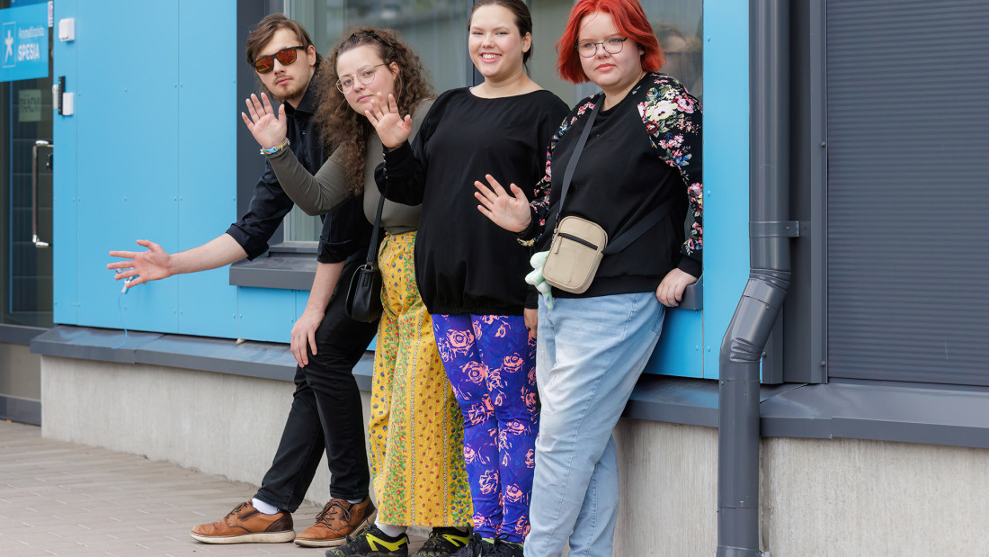 Neljä nuorta seisovat seinän edessä ja moikkaavat.