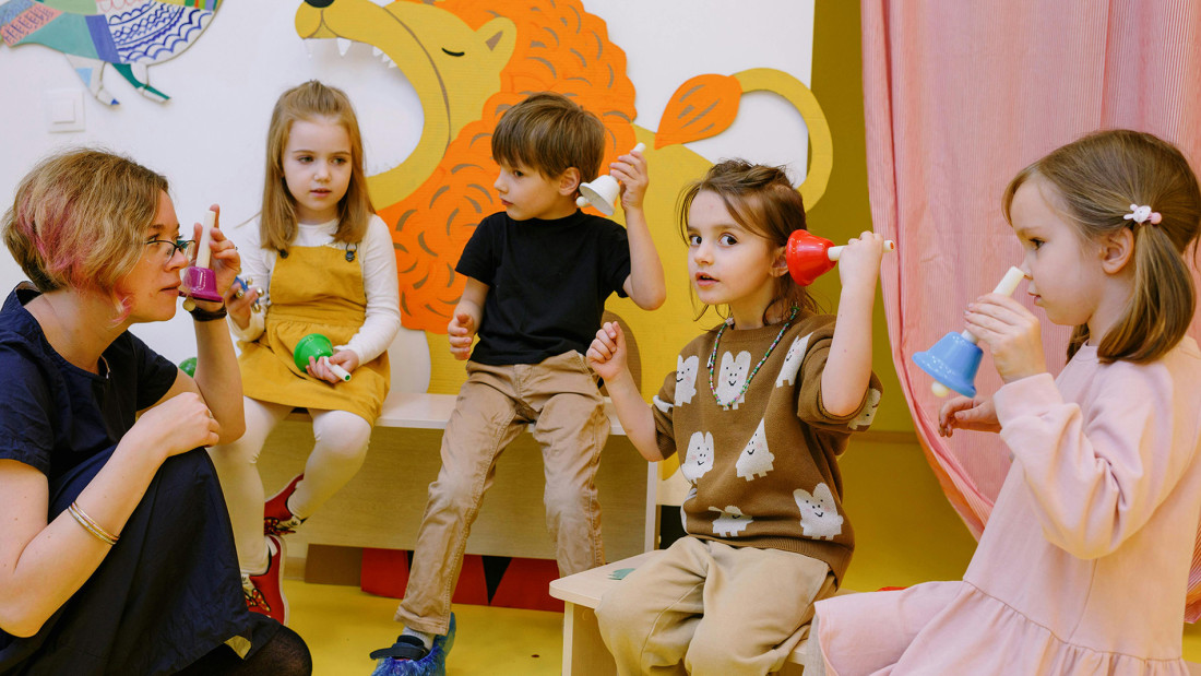 Neljä lasta ja aikuinen pitelevät soittokelloja ja kuuntelevat niitä.