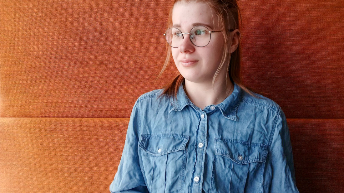 Nuori nainen seisoo ruskean seinän edessä tyynen näköisenä.