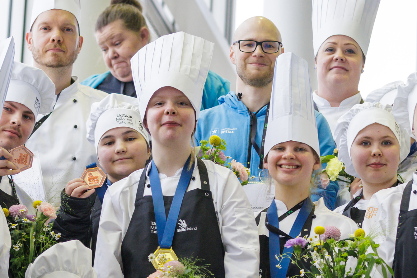 Kokkiasuihin pukeutuneita henkilöitä ryhmäkuvassa, keskellä Spesian Taitaja2025-mitalistit mitalit kaulassa.
