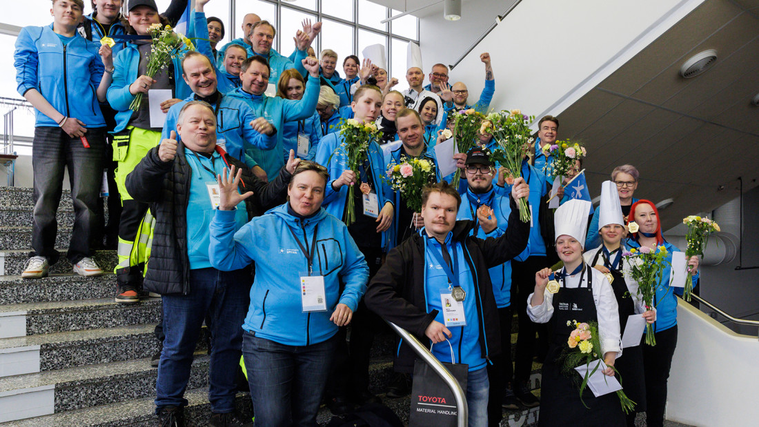 Spesian sinisiin huppareihin pukeutunut iloinen joukko seisoo portaikossa ja tuulettaa Taitaja-mitaleita.