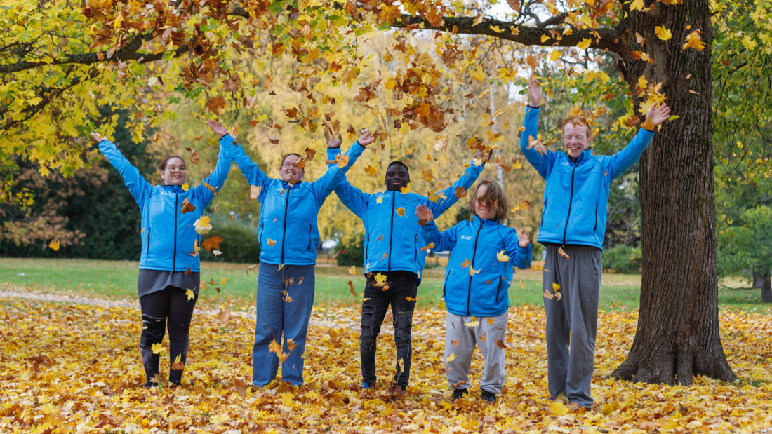 Viisi nuorta Spesian takit päällä syksyisessä maisemassa heittävät keltaisia lehtiä ilmaan.