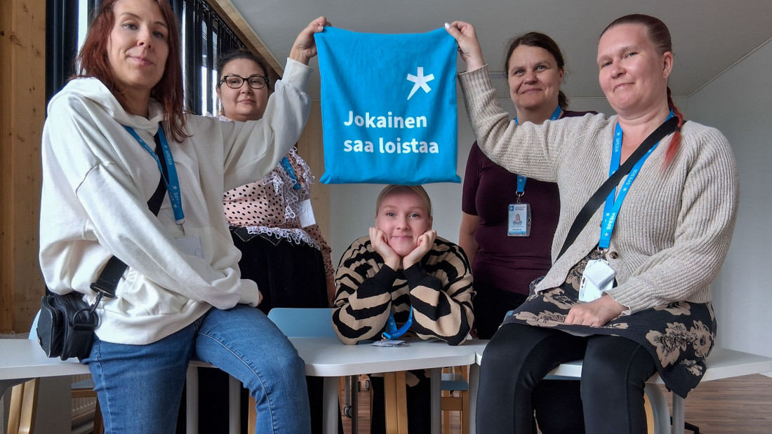 Viisi henkilöä pöydän ympärillä pitelee Spesian kassia.