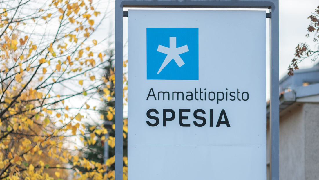 Ammattiopisto Spesian kyltti ulkona syksyisen puun vieressä.