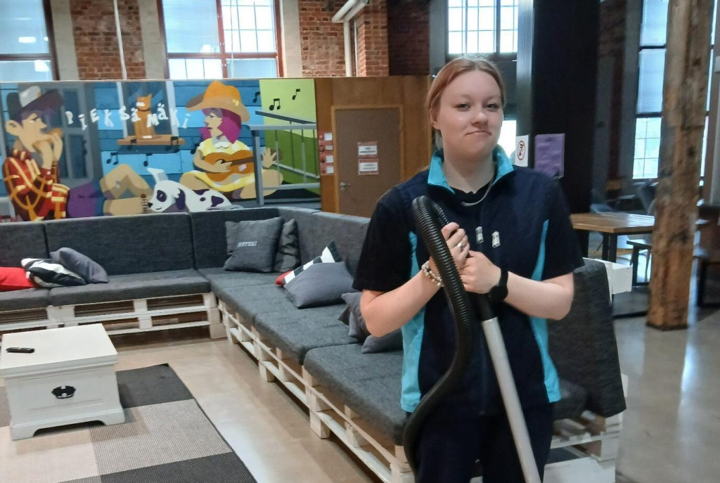 Minttu Laulainen kuvattuna imuri kädessä työvaatteet päällään.
