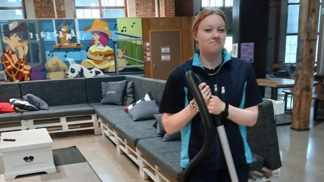 Minttu Laulainen kuvattuna imuri kädessä työvaatteet päällään.