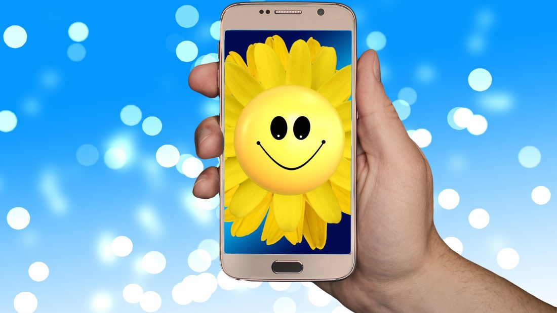 Kännykän ruudulla hymyilevä auringonkukka.