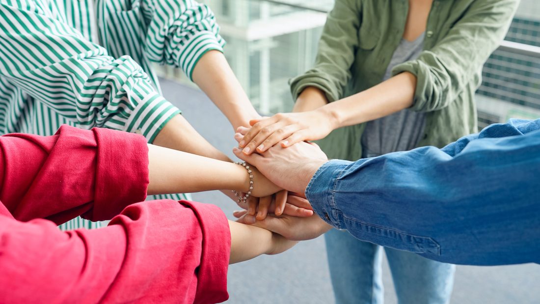 Ihmisiä ringissä pitämässä käsiään keskellä yhteistyön merkiksi.