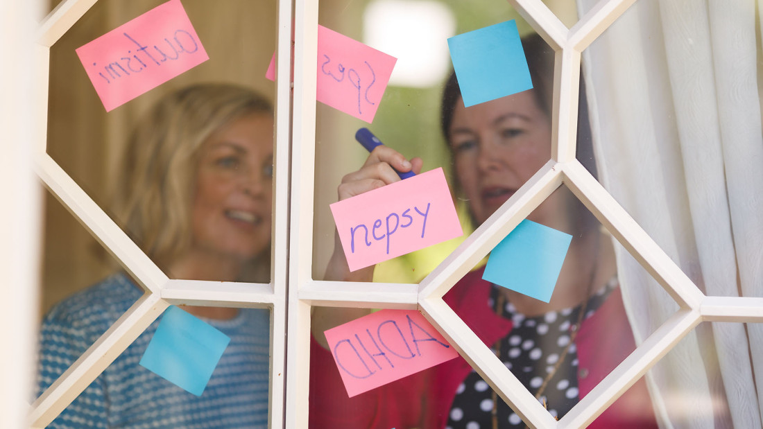 Ikkunan läpi kuvatut kaksi henkilöä ovat kirjoittamassa nepsy-aiheisia liimalappuja.