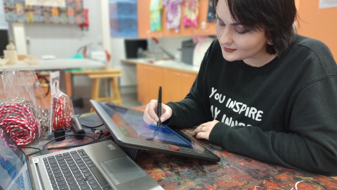 Opiskelija piirtää piirtotabletille, vieressä käsintehtyjä tuotteita.