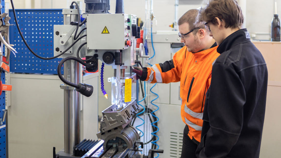 Opiskelijat työvaatteissa tutkivat työkonetta.