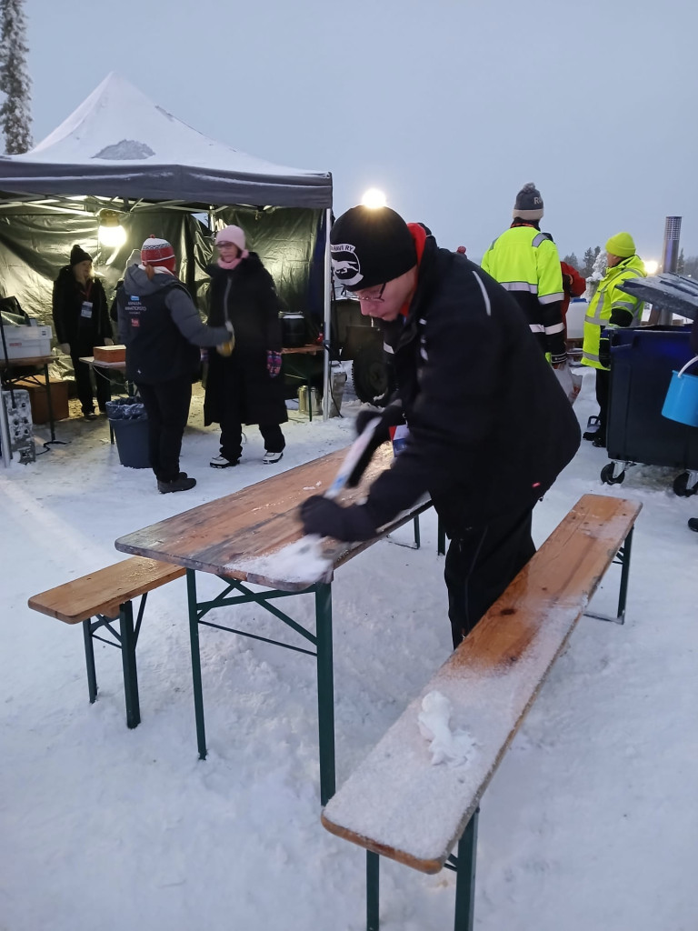 Henkilö poistaa lunta ja jäätä penkiltä. 