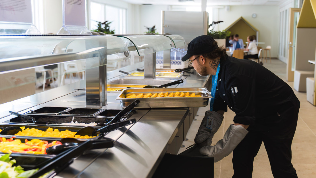 Henkilö asettaa uutta lounasannosta tarjolle lounaslinjastolla.