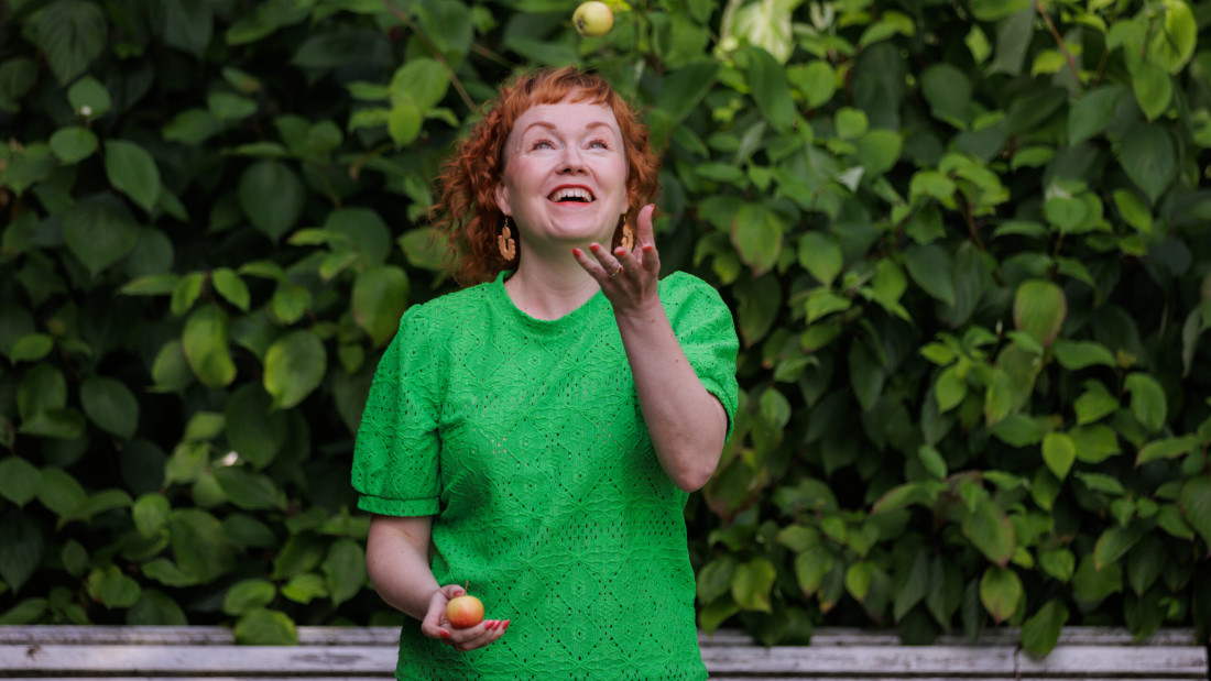 Punahiuksinen nainen jonglööraa omenoilla.