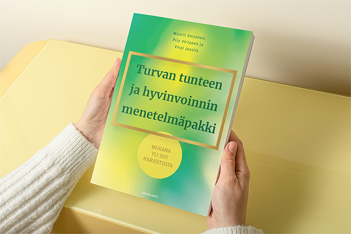 Kädet pitelevät Turvan tunteen ja hyvinvoinnin menetelmäpakki -kirjaa.