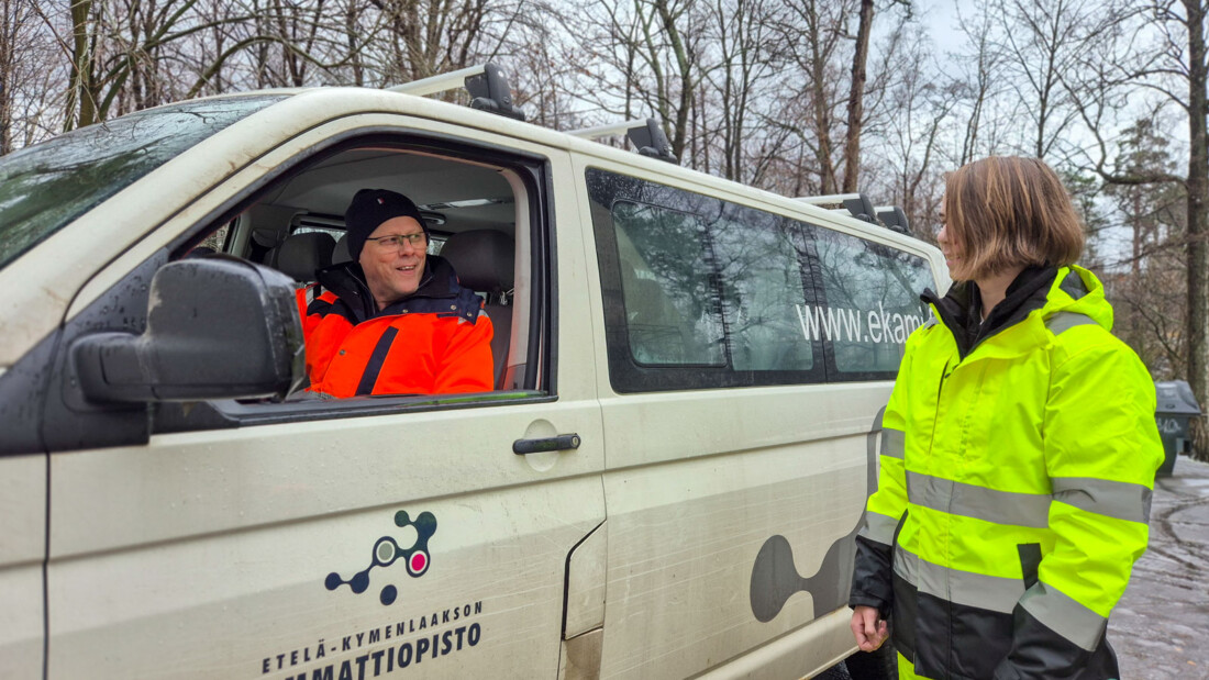 Kaksi henkilöä juttelee. Vanhempi istuu ikkuna auki pakettiautossa ja nuorempi seisoo sen vieressä.