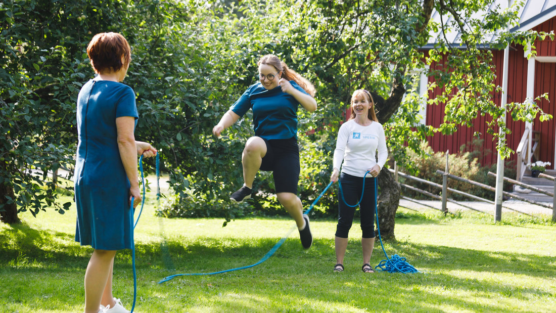 Kaksi henkilöä pyörittää hyppynarua kolmannen hyppiessä aurinkoisena kesäpäivänä.