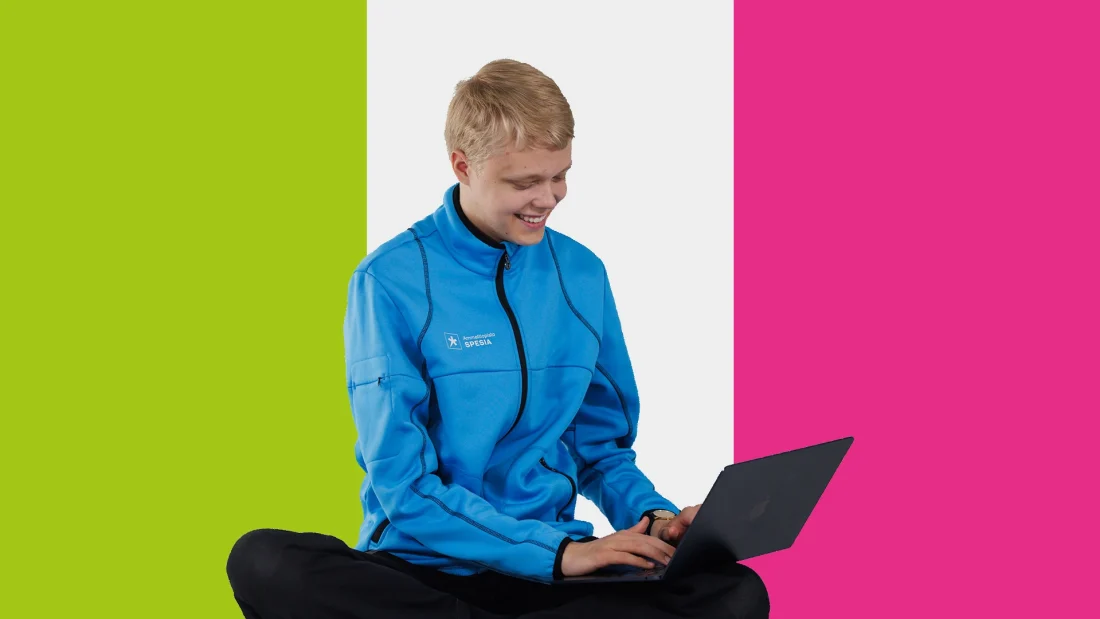 Spesian takkiin pukeutunut nuori mies istuu risti-istunnassa läppäri sylissään.