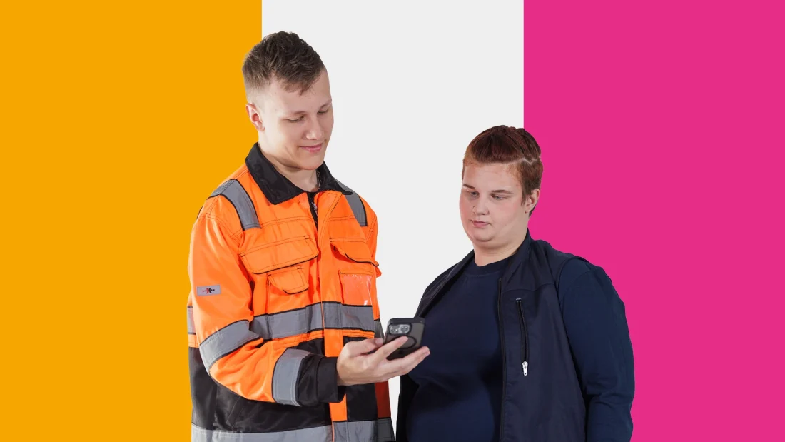 Kaksi työasuihin pukeutunutta nuorta tutkii kännykkää.