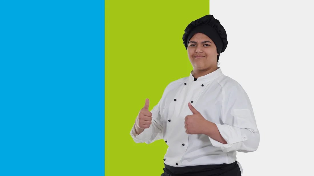 Kokin asuun pukeutunut nuori nainen nostaa peukkuja ja hymyilee.