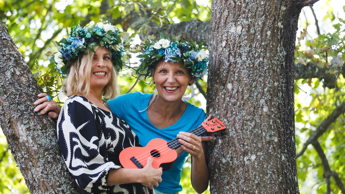 Tuula Niskanen ja Virpi Jussila ovat puussa ja soittavat kitaraa.