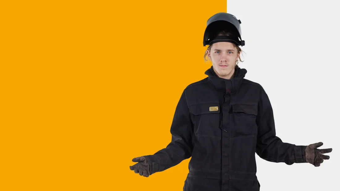 Hitsausasuun ja -kypärään pukeutunut nuori seisoo kädet levällään.