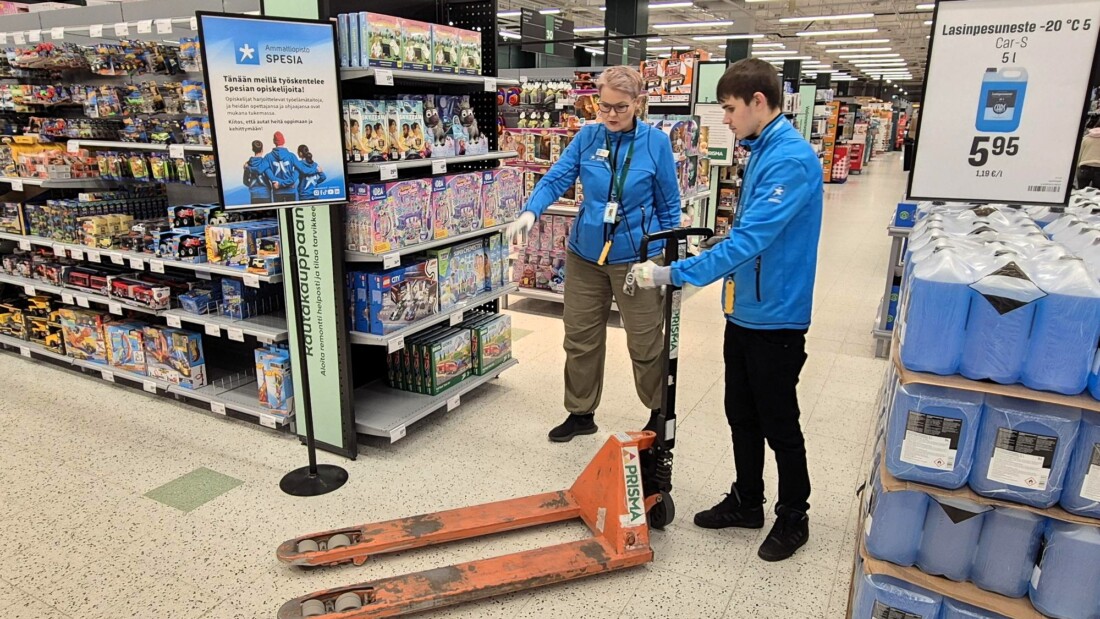 Spesian opiskelija ja opettaja Prisman käytävällä harjoittelemassa lavan siirtoa pumppukärryllä.