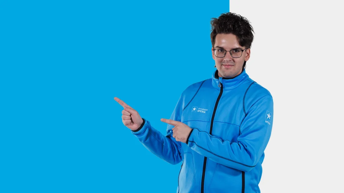 Spesian takkiin pukeutunut nuori osoittaa molemmilla etusormillaan sivulle.