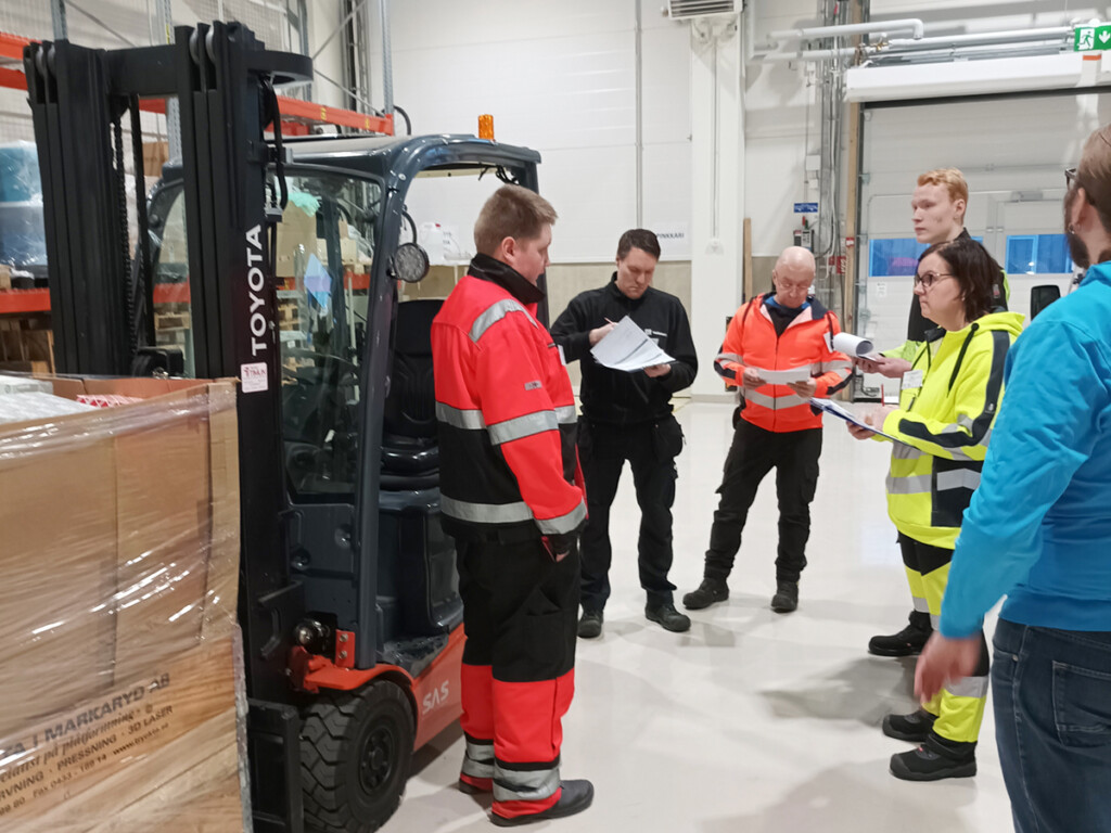 Taitaja-semien P-logistiikan kisatilanne, jossa tuomareita ja kilpailija seisovat trukin vierellä.